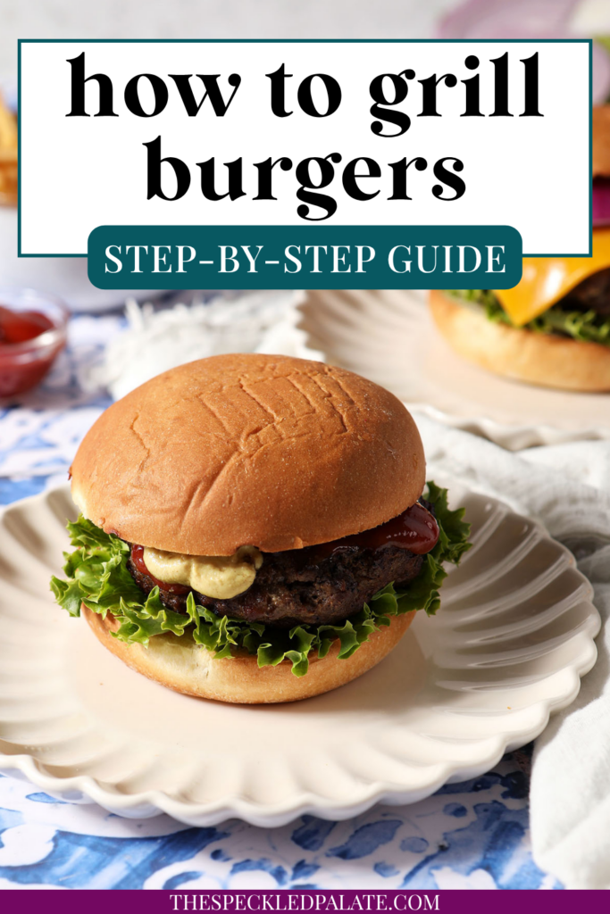 A dressed grilled hamburger sits on a plate on a blue tiled surface.