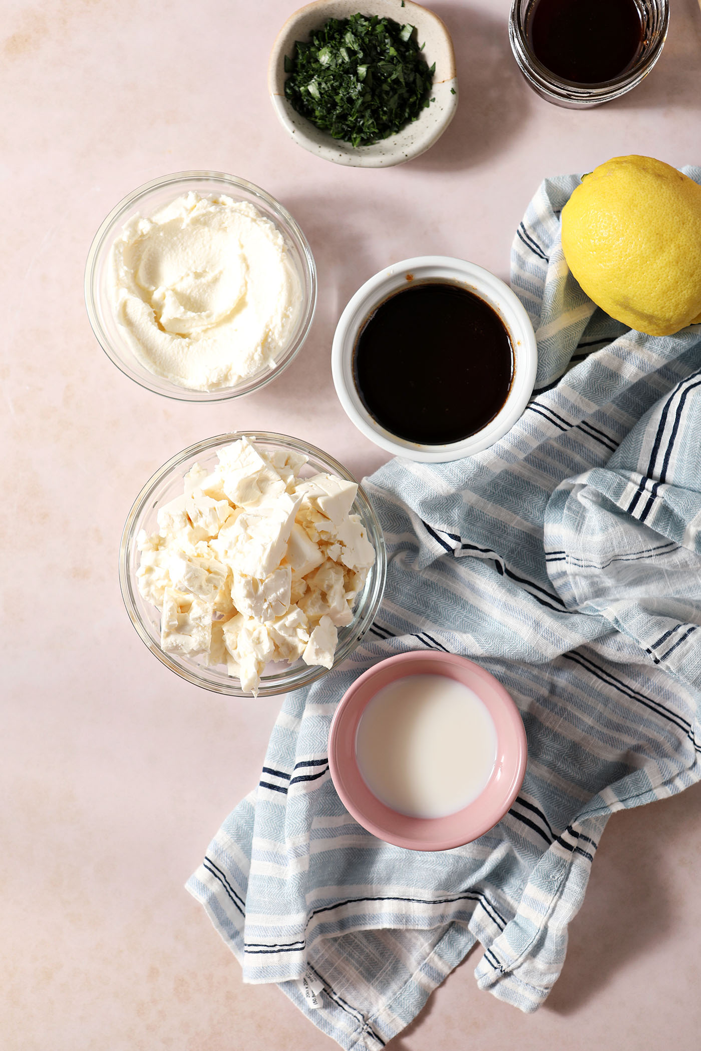 Ingredients to make a dip with whipped feta, ricotta, and hot honey in bowls on a brown surface with a blue striped linen