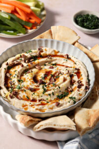 Hot honey dip, garnished with more hot honey, chopped pecans, chopped herbs and lemon zest, in a gray bowl with fresh pita