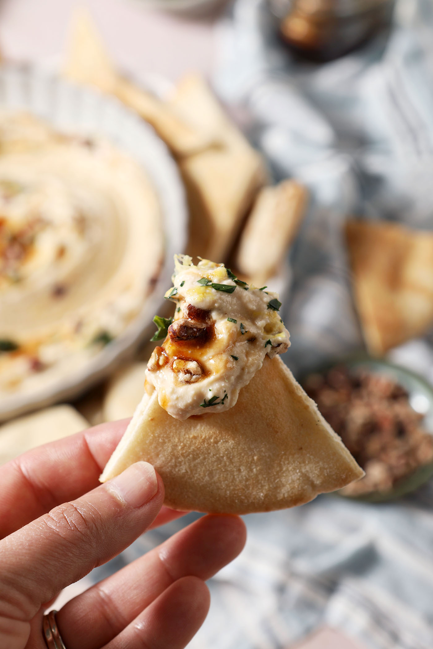 A pita triangle holds a bite of hot honey dip above a platter.