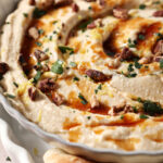 Close-up of hot honey dip with chopped herbs, hot honey, chopped pecans and lemon zest in a gray bowl.
