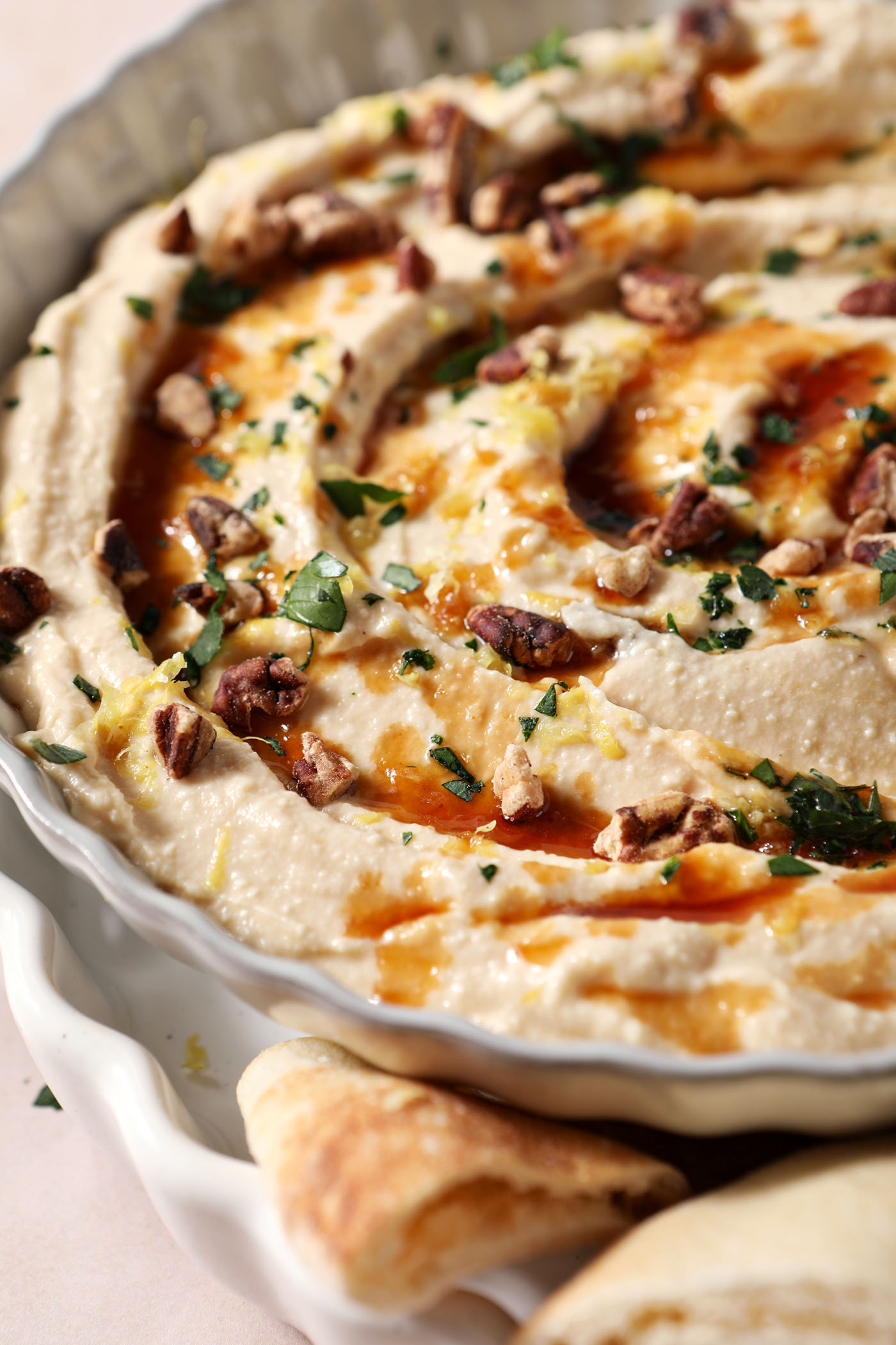 Close-up of hot honey dip with chopped herbs, hot honey, chopped pecans and lemon zest in a gray bowl.