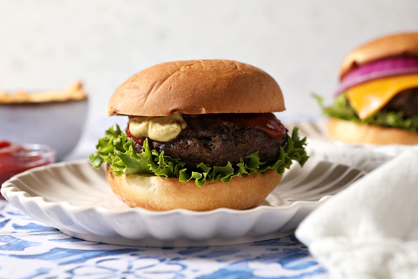 A dressed grilled hamburger sits on a plate on a blue tiled surface.