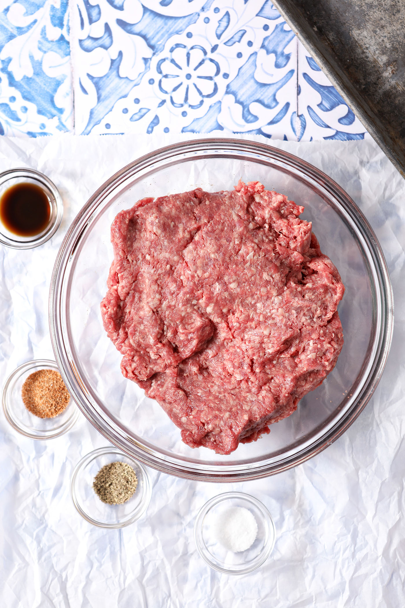Ground beef in a bowl surrounded by seasonings.
