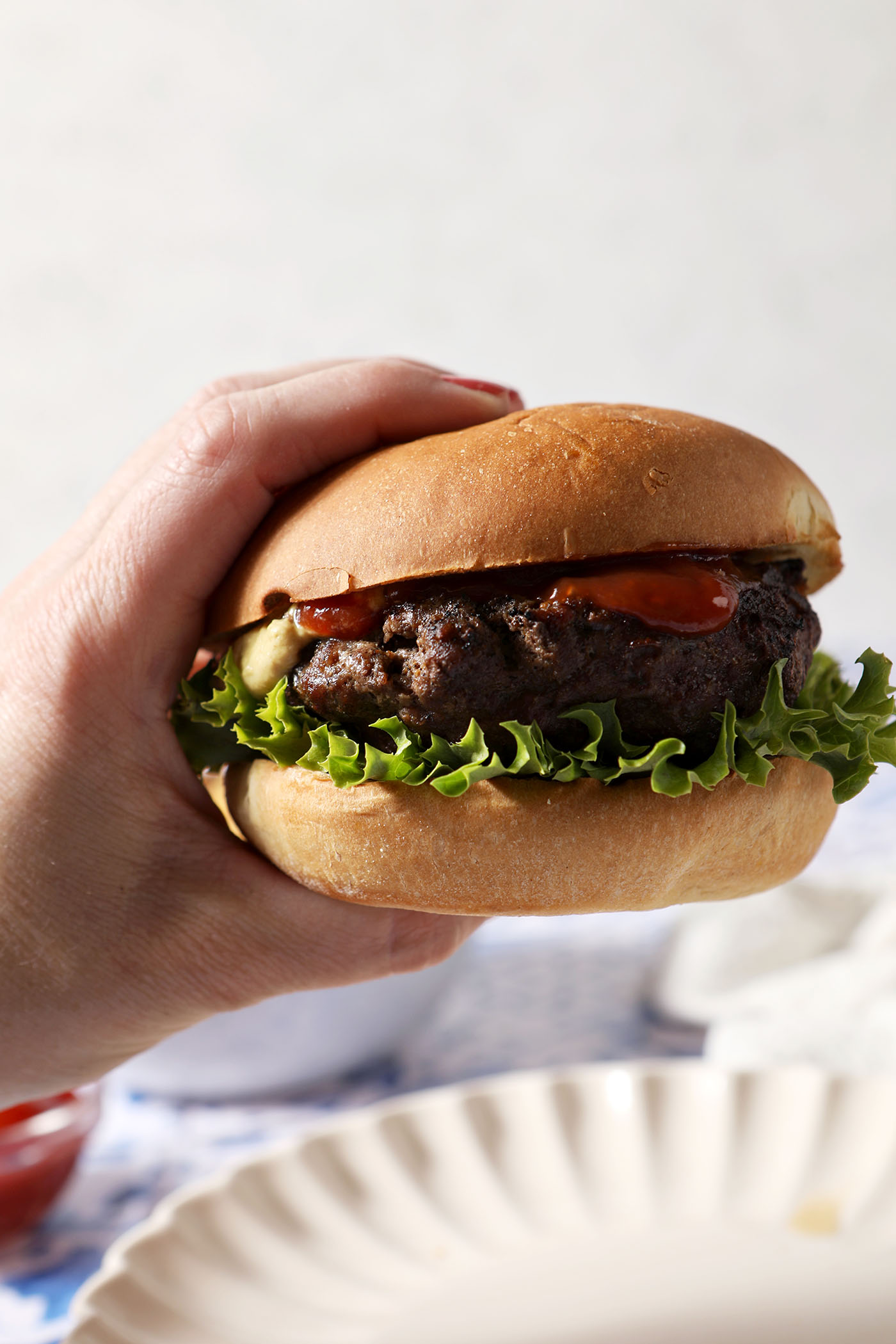 A hand holds a grilled burger up in front of a white surface.