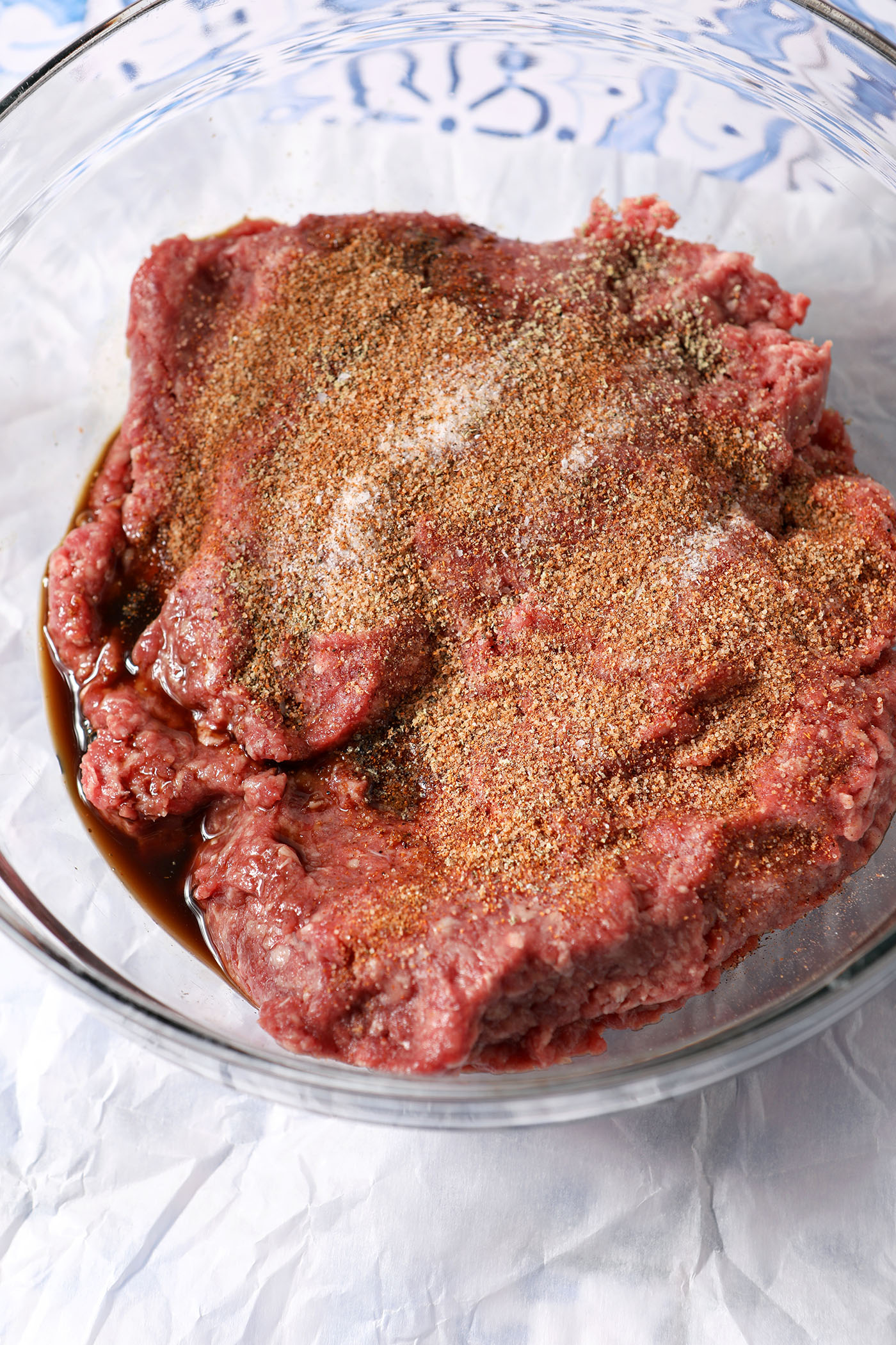 Ground beef in a bowl, seasoned with Cajun seasoning, salt, and pepper.