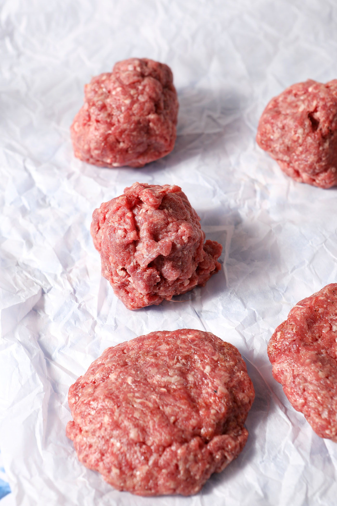 Burger patties partially formed on a sheet of parchment paper.