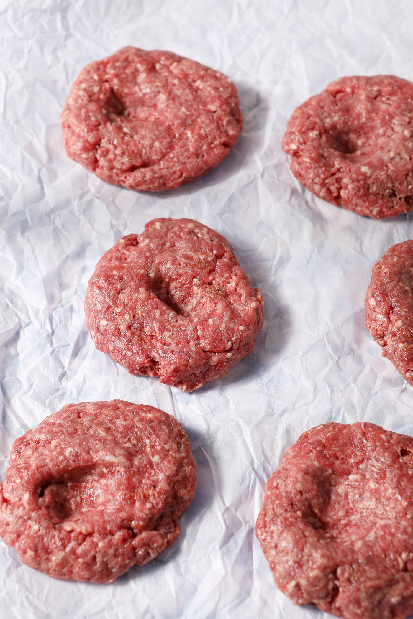 Burger patties with indentations in them on parchment paper before grilling