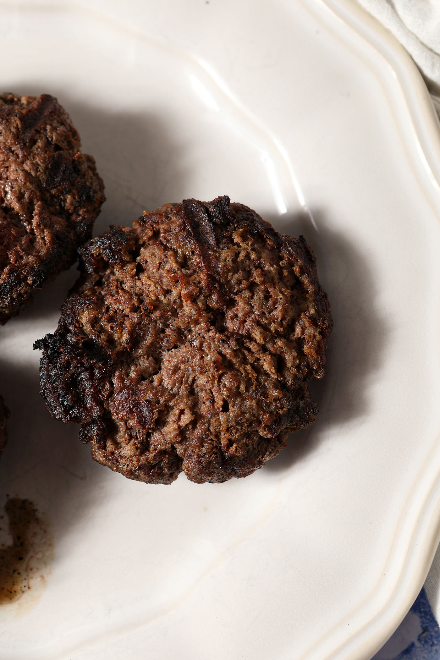 Three grilled beef burgers on a white plate.