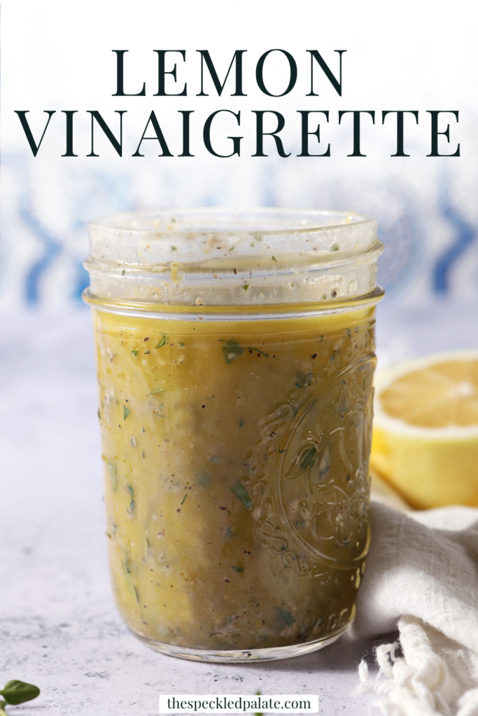 A mason jar of lemon vinaigrette on a stone surface in front of a blue and white tiled backsplash that reads "Lemon Vinaigrette"