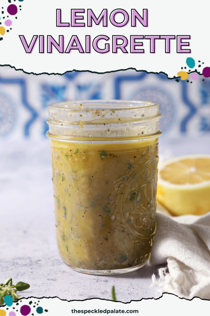 A mason jar of lemon vinaigrette on a stone surface in front of a blue and white tiled backsplash that reads "Lemon Vinaigrette"