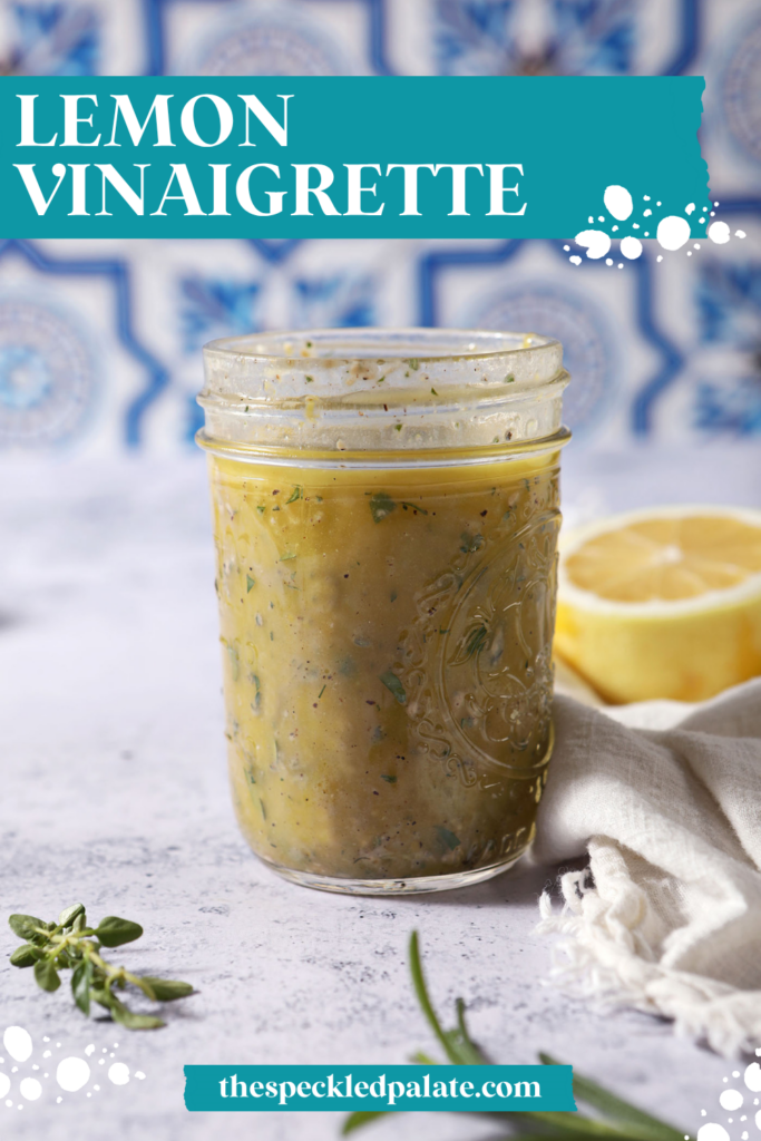 A mason jar of lemon vinaigrette on a stone surface in front of a blue and white tiled backsplash that reads "Lemon Vinaigrette"