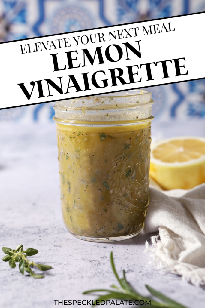 A mason jar of lemon vinaigrette on a stone surface in front of a blue and white tiled backsplash that reads "Lemon Vinaigrette"