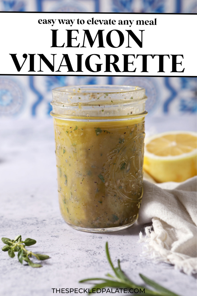 A mason jar of lemon vinaigrette on a stone surface in front of a blue and white tiled backsplash that reads "Lemon Vinaigrette"