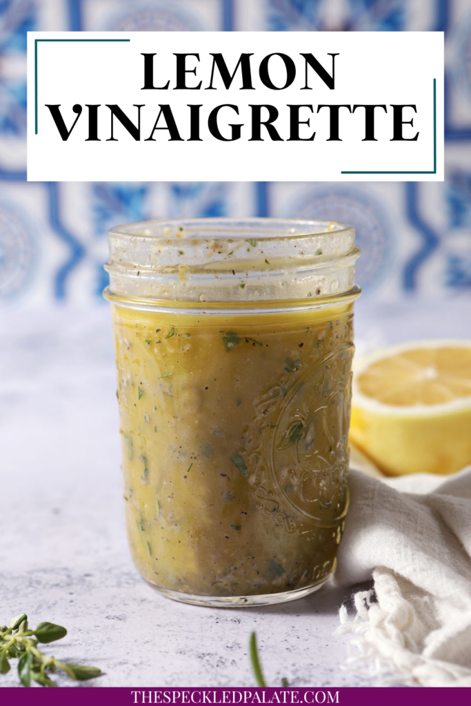 A mason jar of lemon vinaigrette on a stone surface in front of a blue and white tiled backsplash that reads "Lemon Vinaigrette"