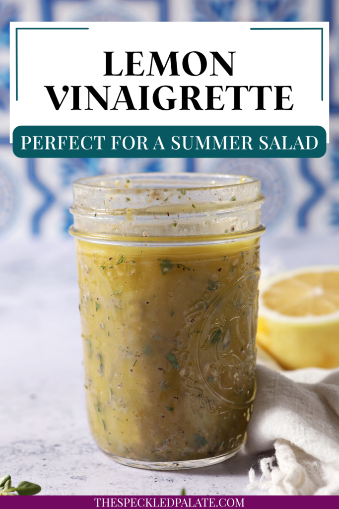 A mason jar of lemon vinaigrette on a stone surface in front of a blue and white tiled backsplash that reads "Lemon Vinaigrette"