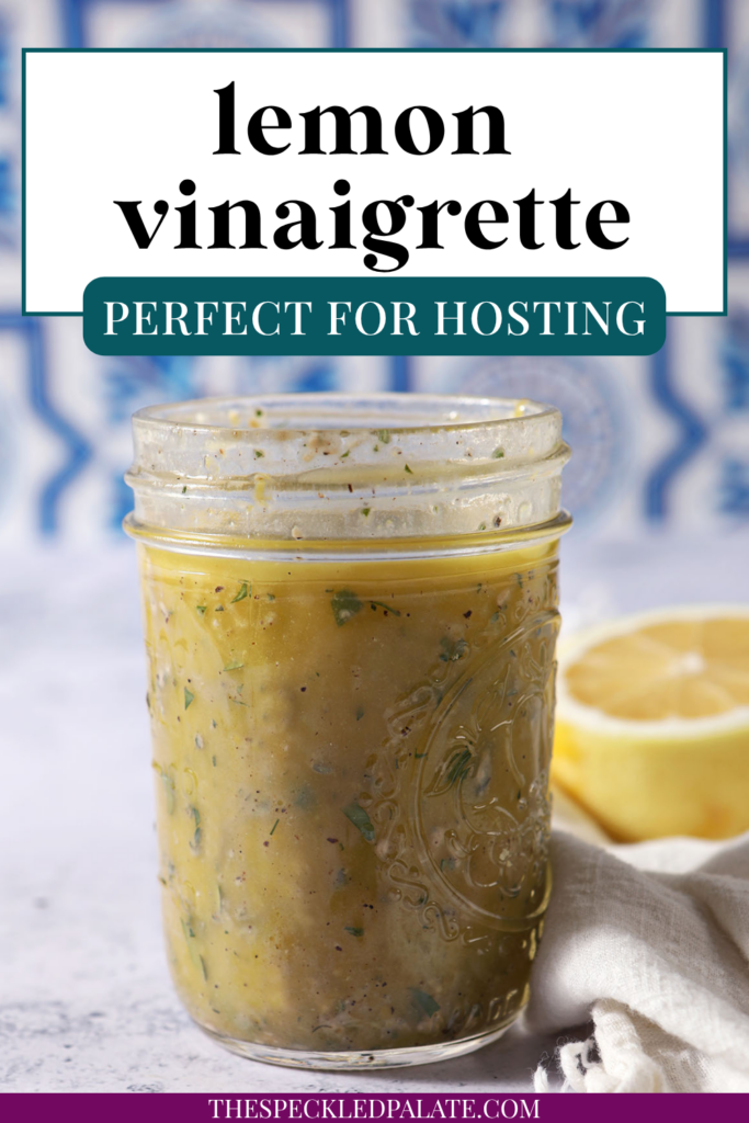 A mason jar of lemon vinaigrette on a stone surface in front of a blue and white tiled backsplash that reads "Lemon Vinaigrette"