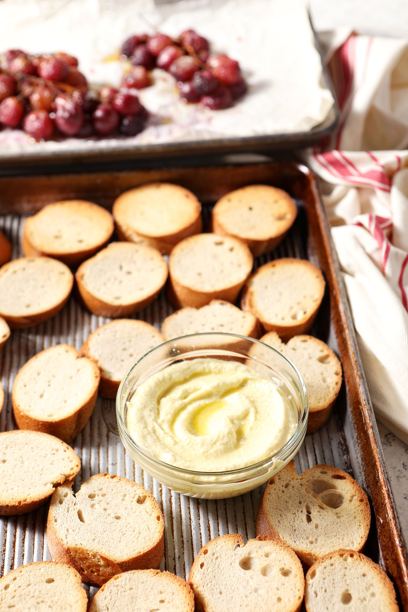 Crostini on a sheet pan with a bowl of whipped feta before the bruschetta are assembled