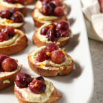 Side angle of Roasted Grape Bruschetta with Whipped Feta on a white platter