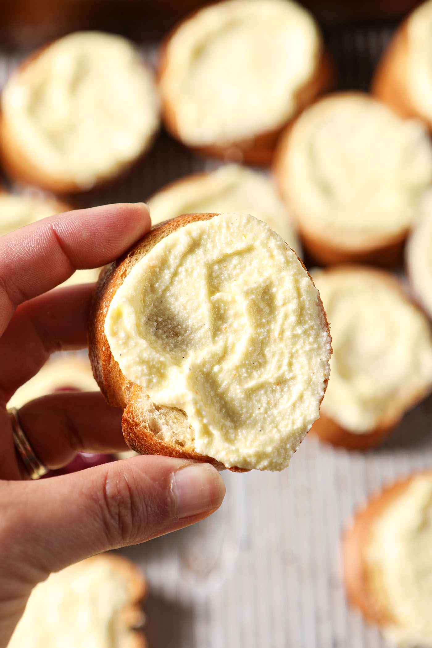 A hand holds a crostini smeared with whipped feta