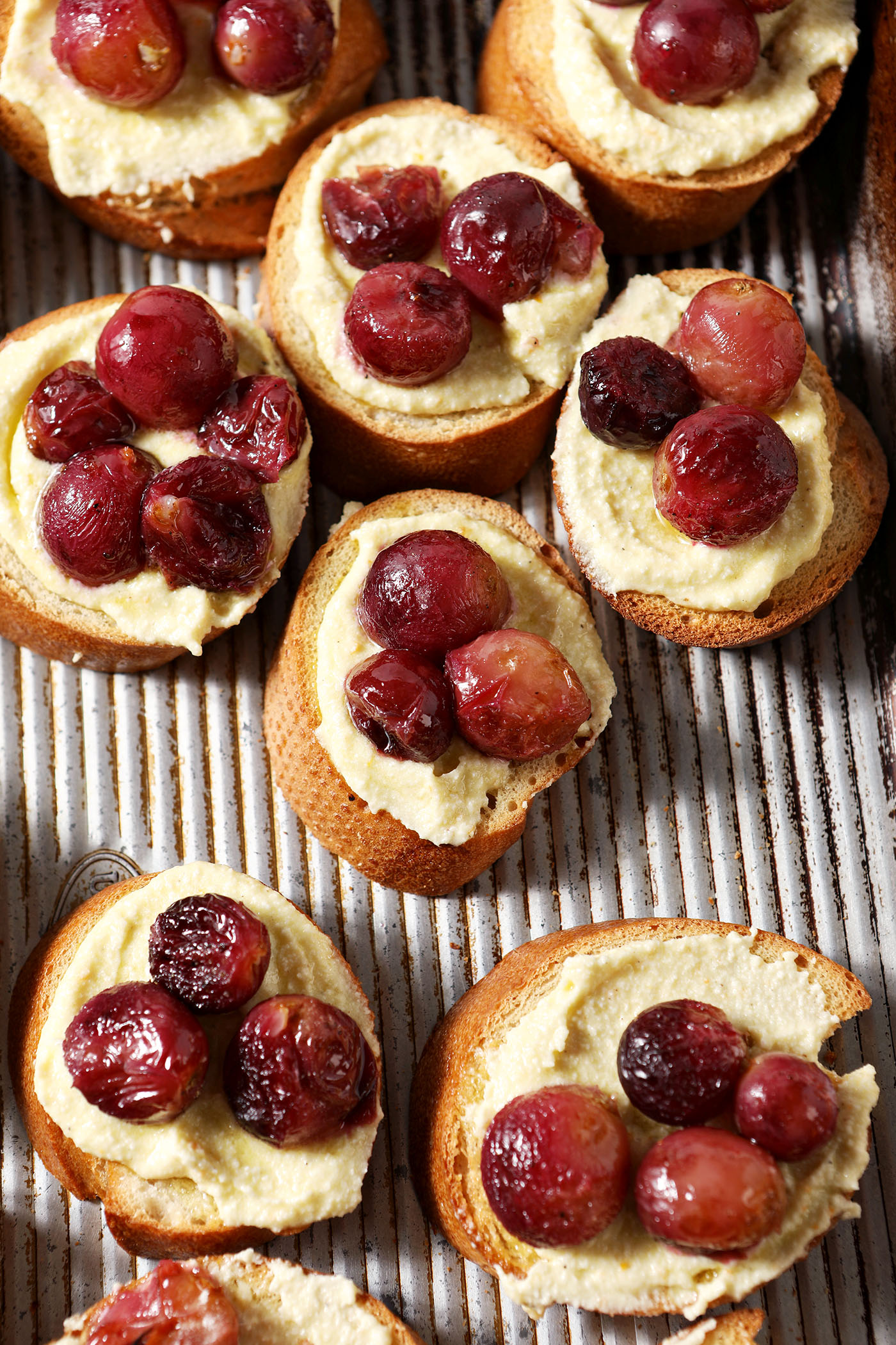 Roasted grape crostini on a sheet pan, before garnished with orange zest