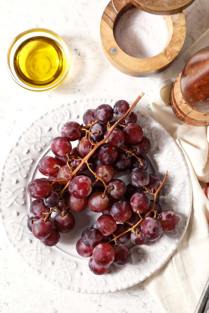 Red grapes on a white plate surrounded by a bowl of oil, salt and pepper