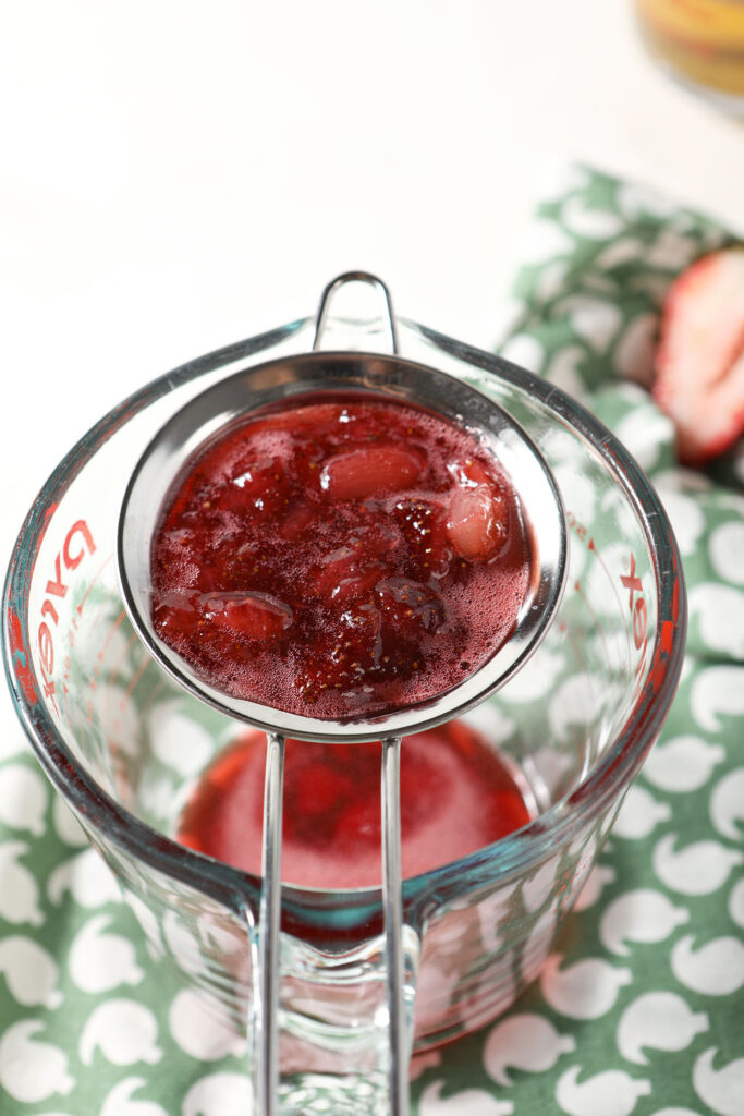 Strawberry syrup strains through a fine mesh sieve into a liquid measuring cup