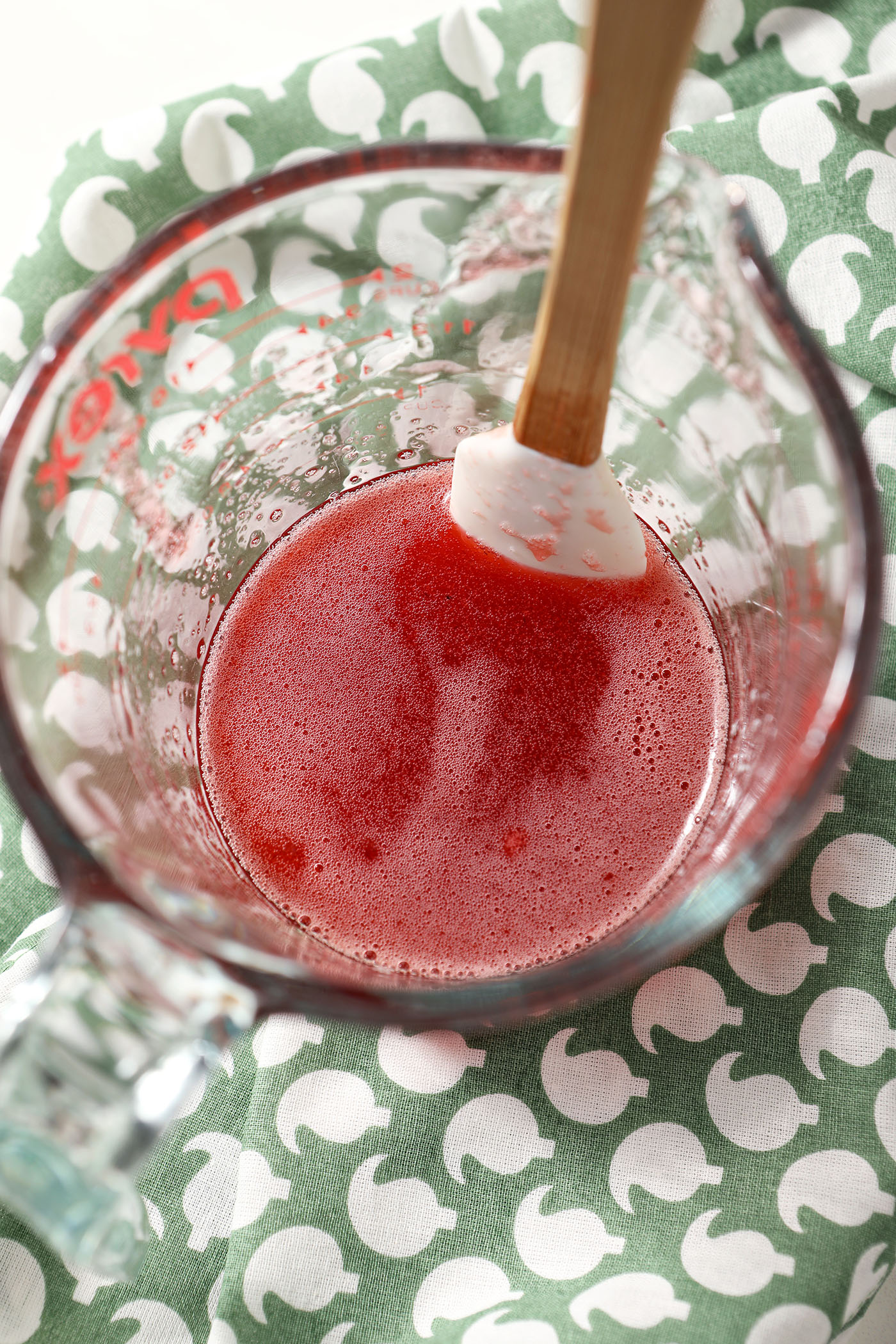 Strawberry shrub syrup in a liquid measuring cup with a rubber spatula