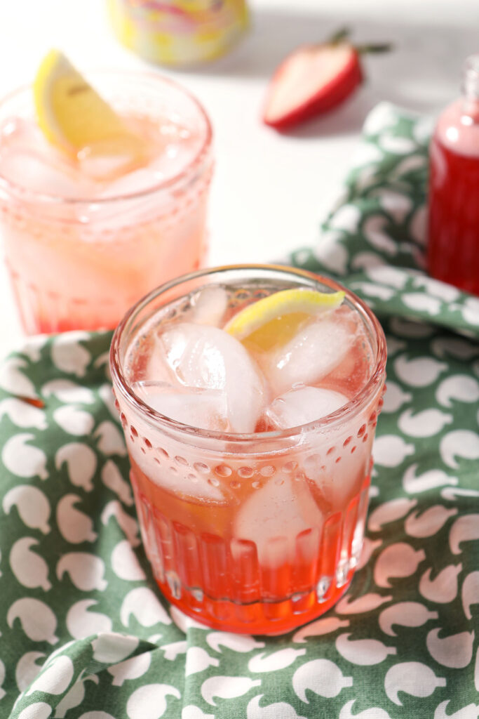 Two glasses of strawberry shrub in a marble surface with a green patterned linen