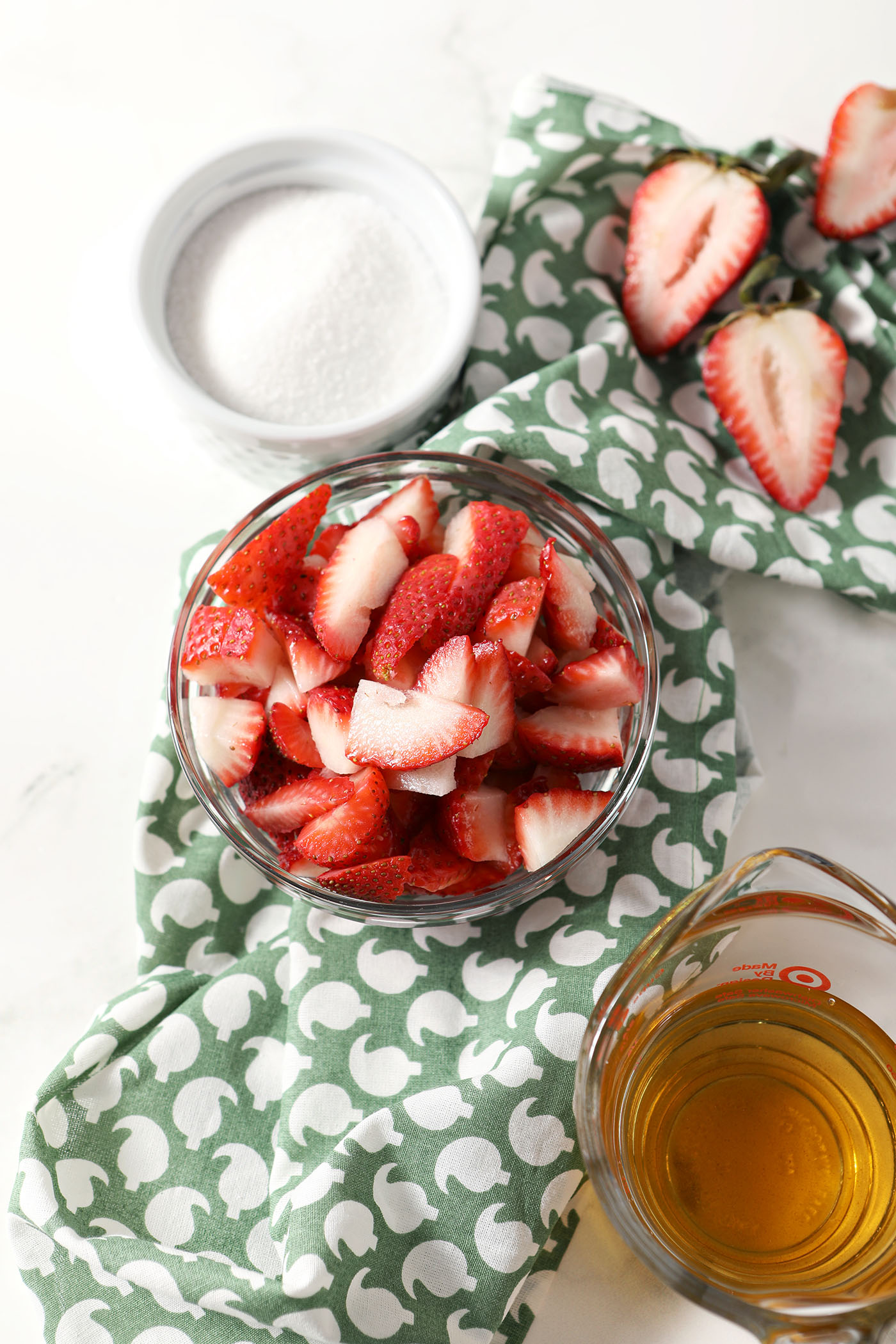 Ingredients to make a shrub with fresh strawberries in bowls on a green patterned linen