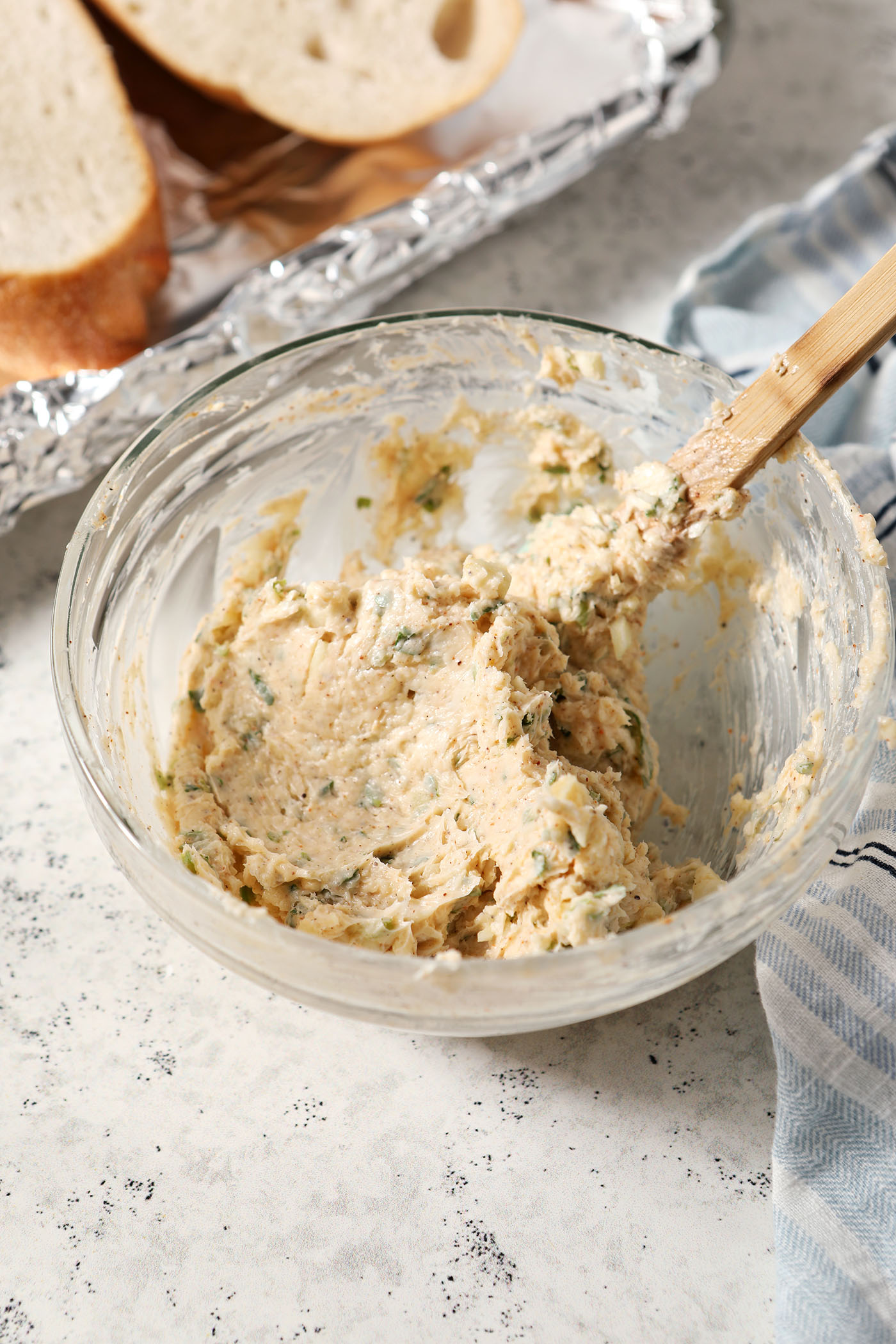 Cajun garlic butter in a bowl with a spatula after mixing, next to a halved loaf of bread