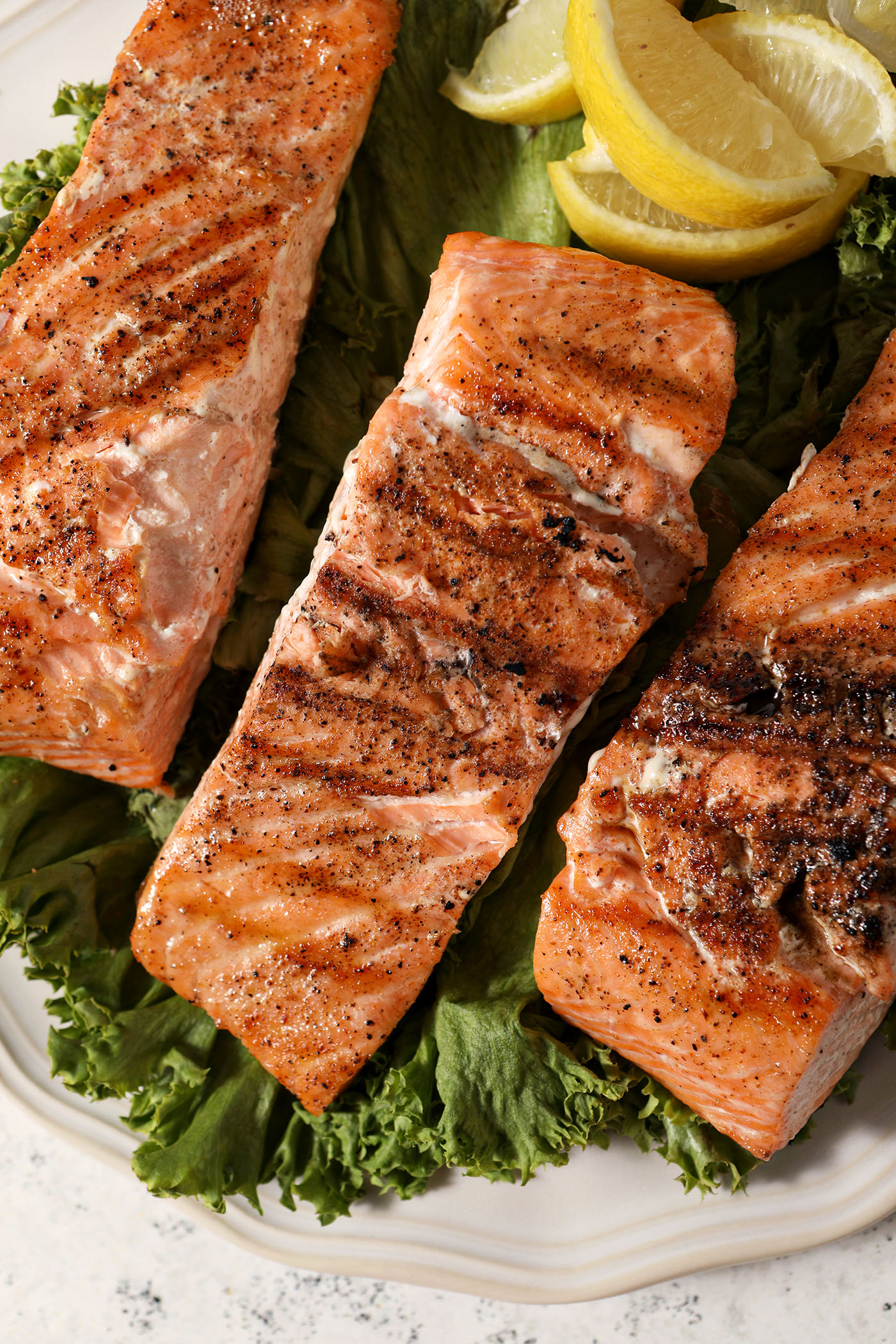 Closeup overhead of grilled salmon on a plate on top of lettuce with lemon slices