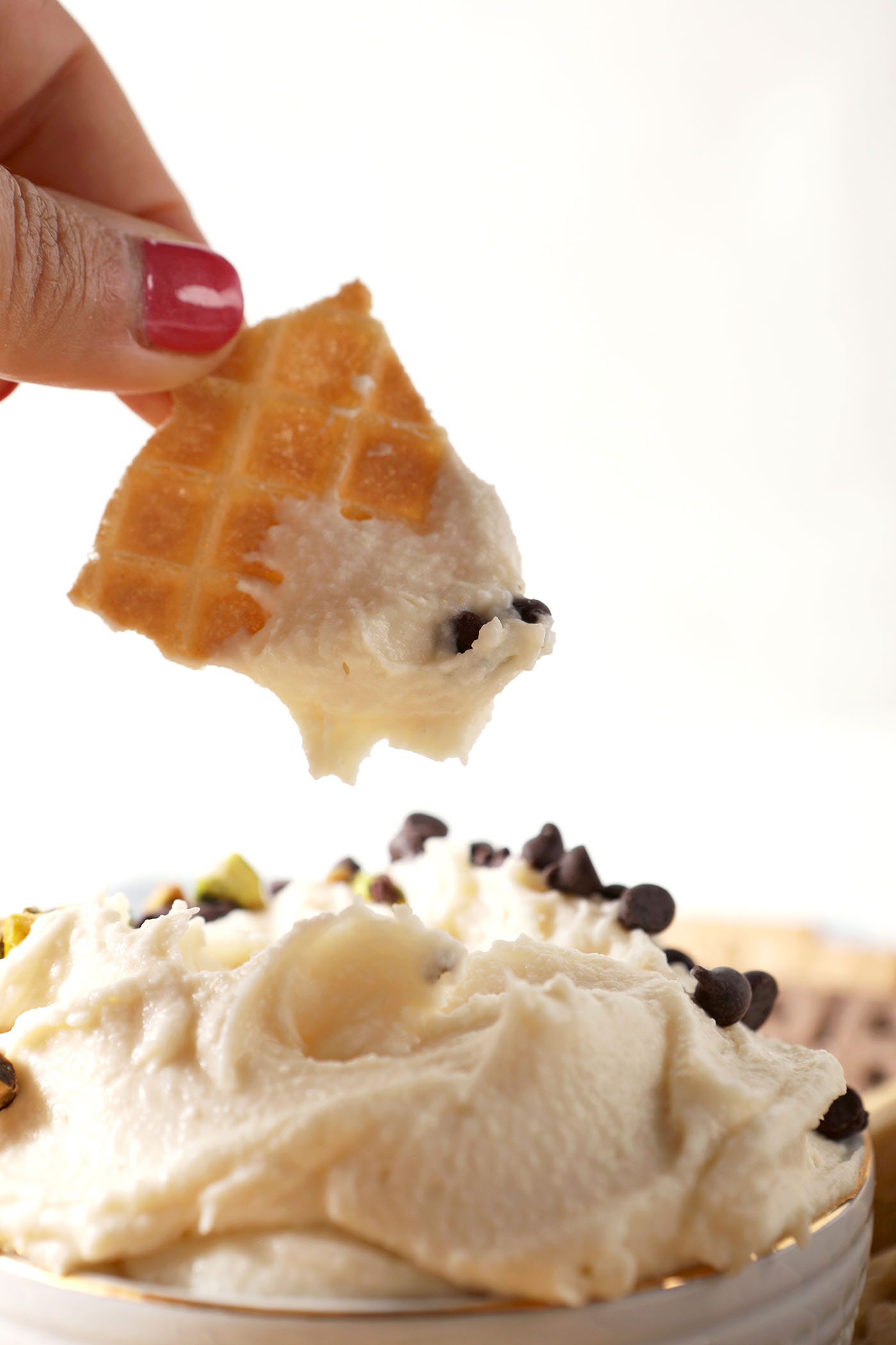 A piece of a waffle cone dips into sweet Cannoli Dip