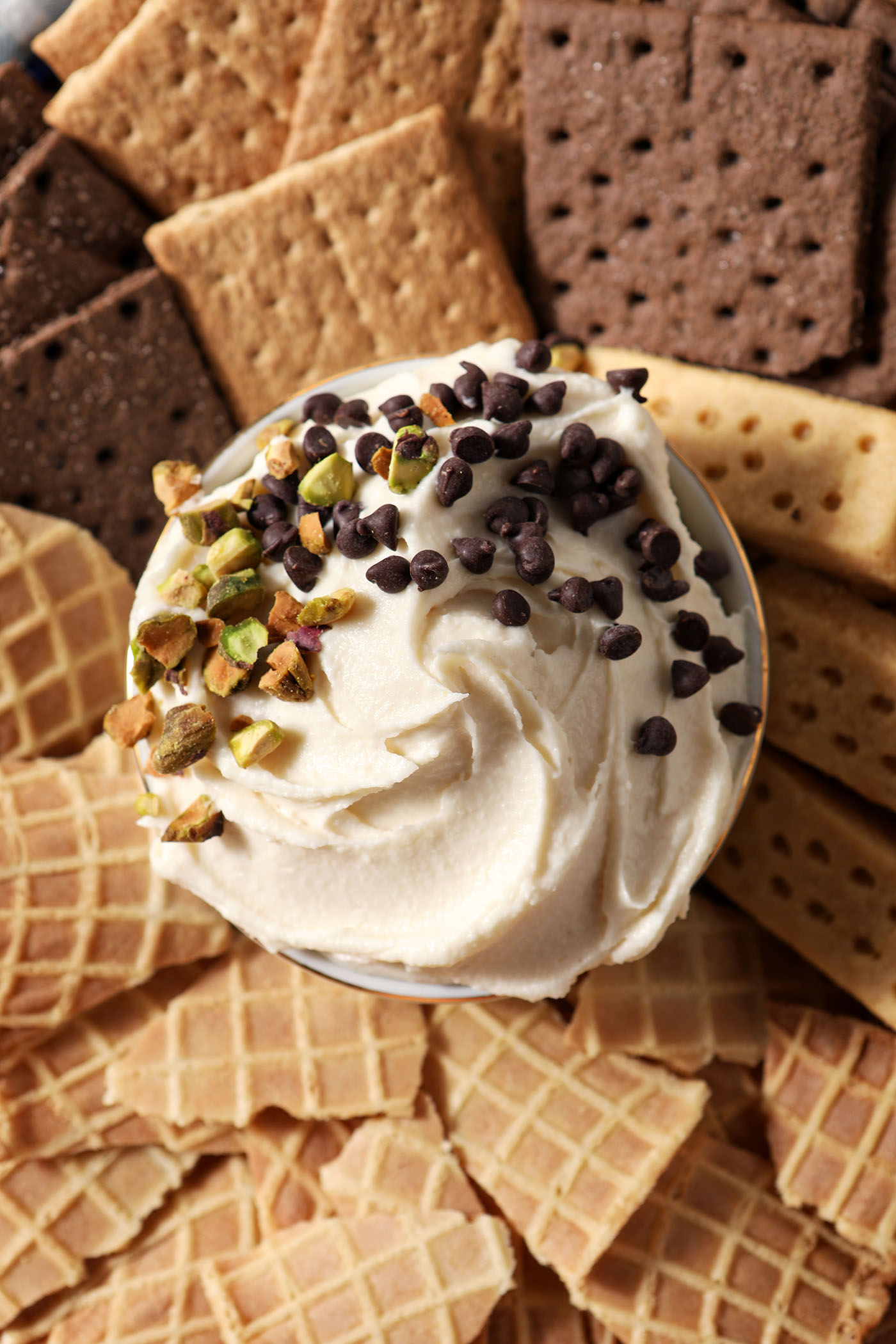 Sweet Cannoli Dip garnished with chopped pistachios and miniature chocolate chips in the middle of various dippers on a platter.