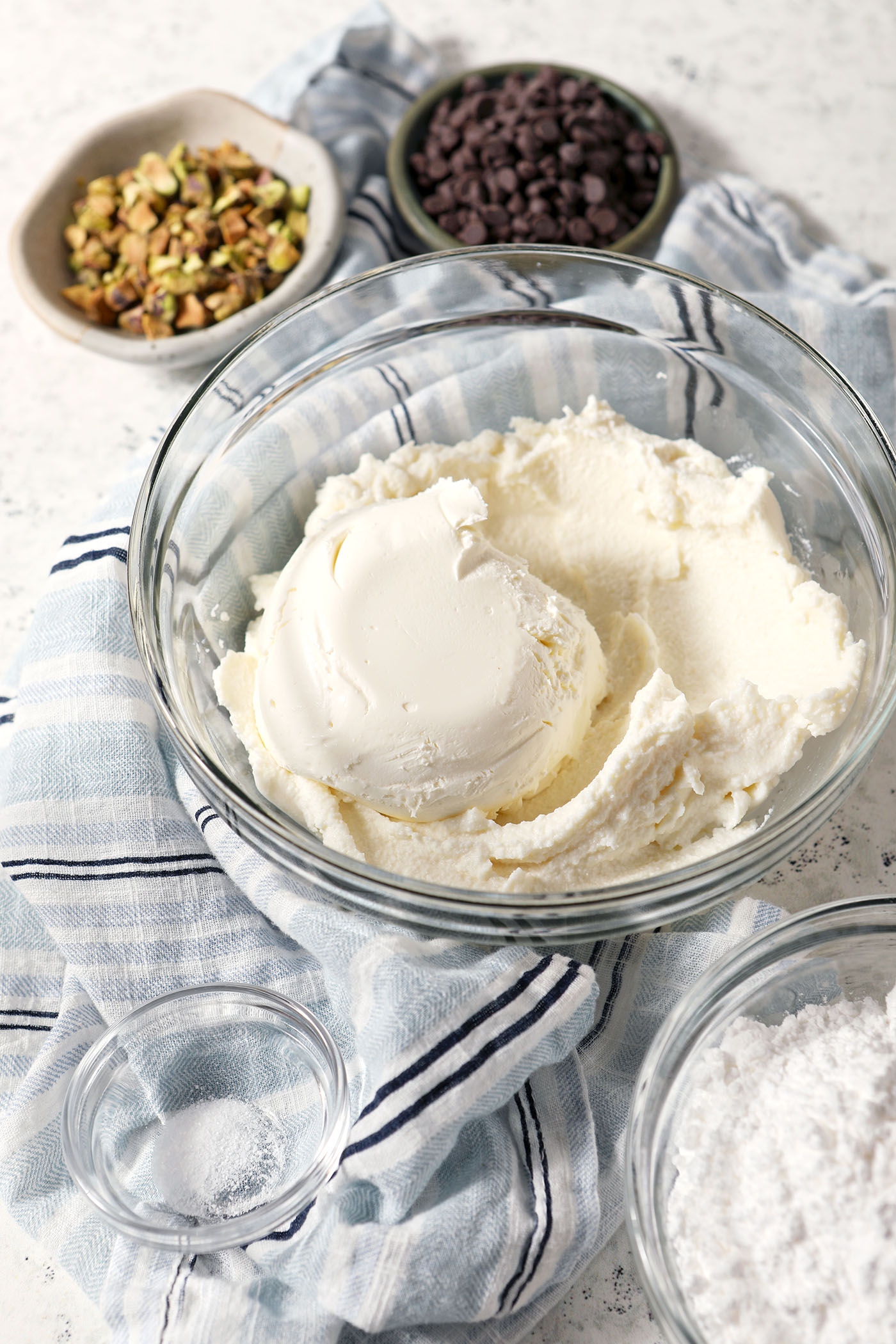Ricotta cheese and marscapone in a bowl before mixing with a blue striped linen on a stone surface