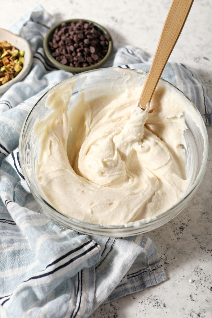 Sweet Cannoli Dip in a mixing bowl after stirring vigorously with a blue striped linen on a stone surface