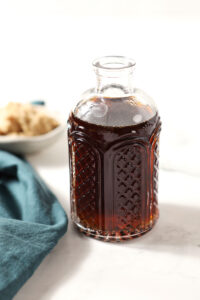 A bottle of brown sugar syrup on a white stone surface next to a turquoise linen
