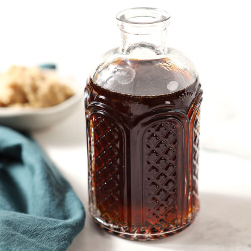 A bottle of brown sugar syrup on a white stone surface next to a turquoise linen