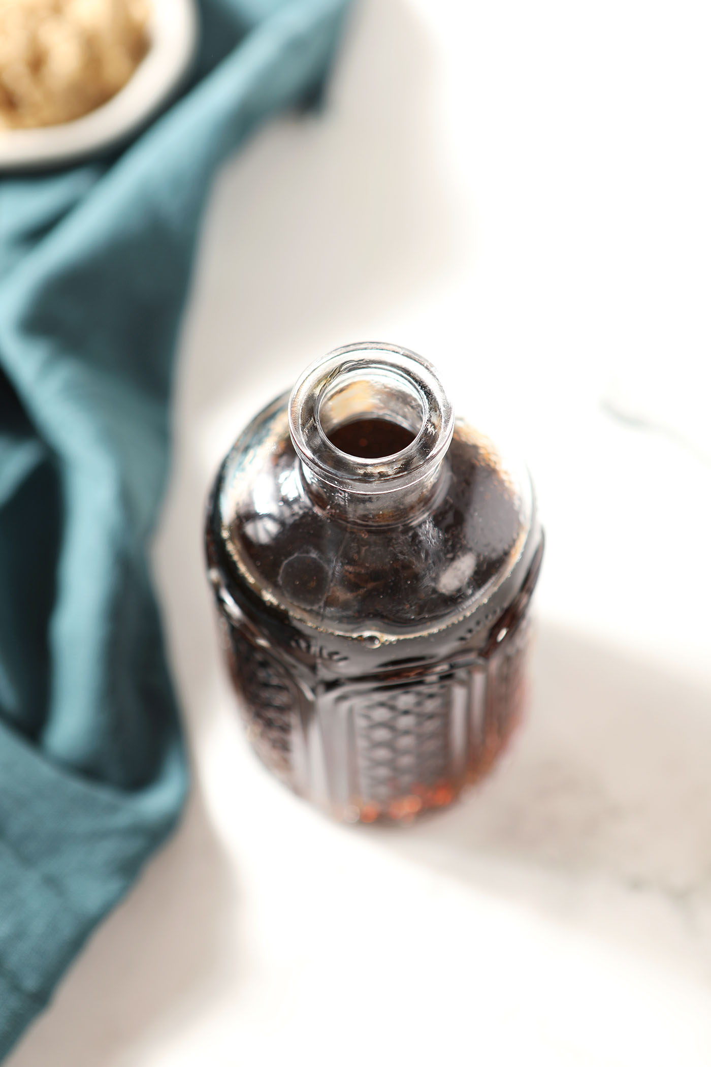 Overhead of a fancy bottle of brown sugar syrup on a stone surface next to a dark turquoise linen