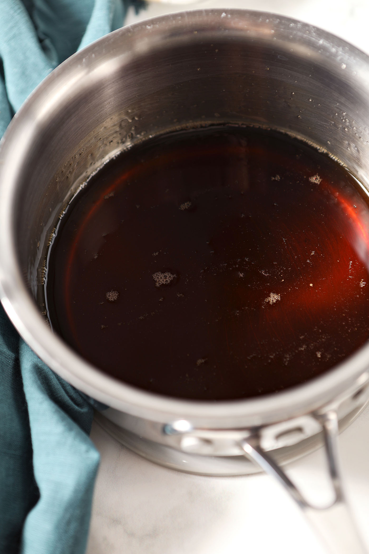 Brown Sugar Simple Syrup in a saucepan, after the sugar melts on a stone surface next to a dark turquoise linen