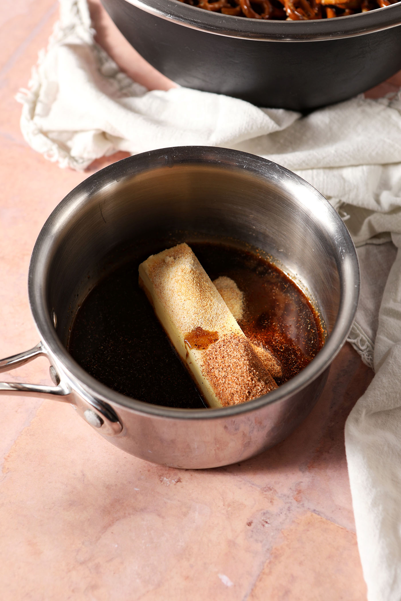 A stick of butter with spices in a small saucepan on a tan brick surface