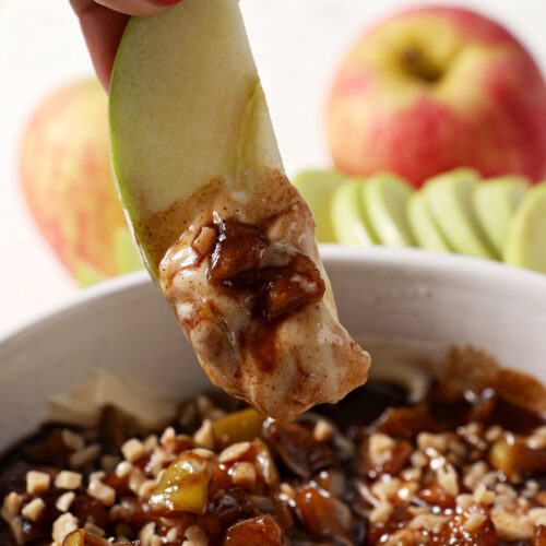 An apple slice dips into a bowl of caramel apple cheesecake dip