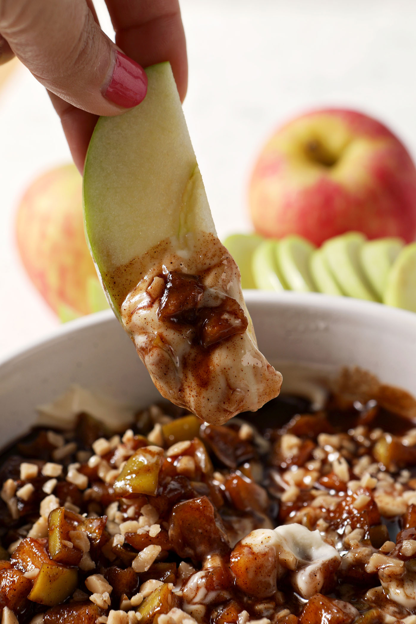 An apple slice dips into a bowl of caramel apple cheesecake dip