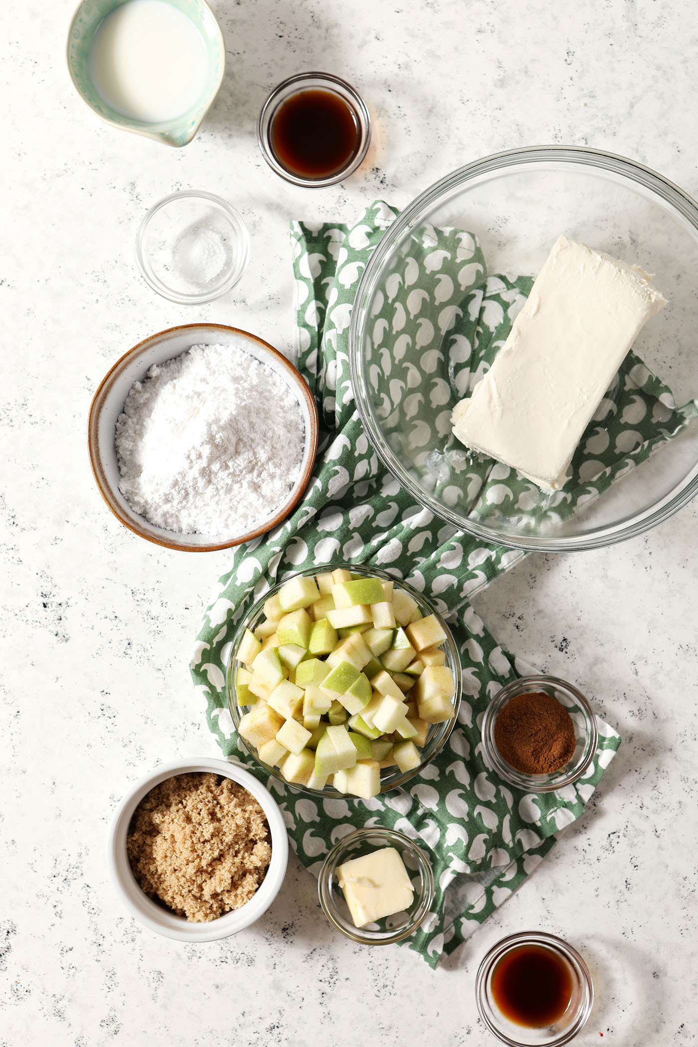 Ingredients to make cheesecake dip and caramelized apples in bowls on a stone surface with a green patterned linen
