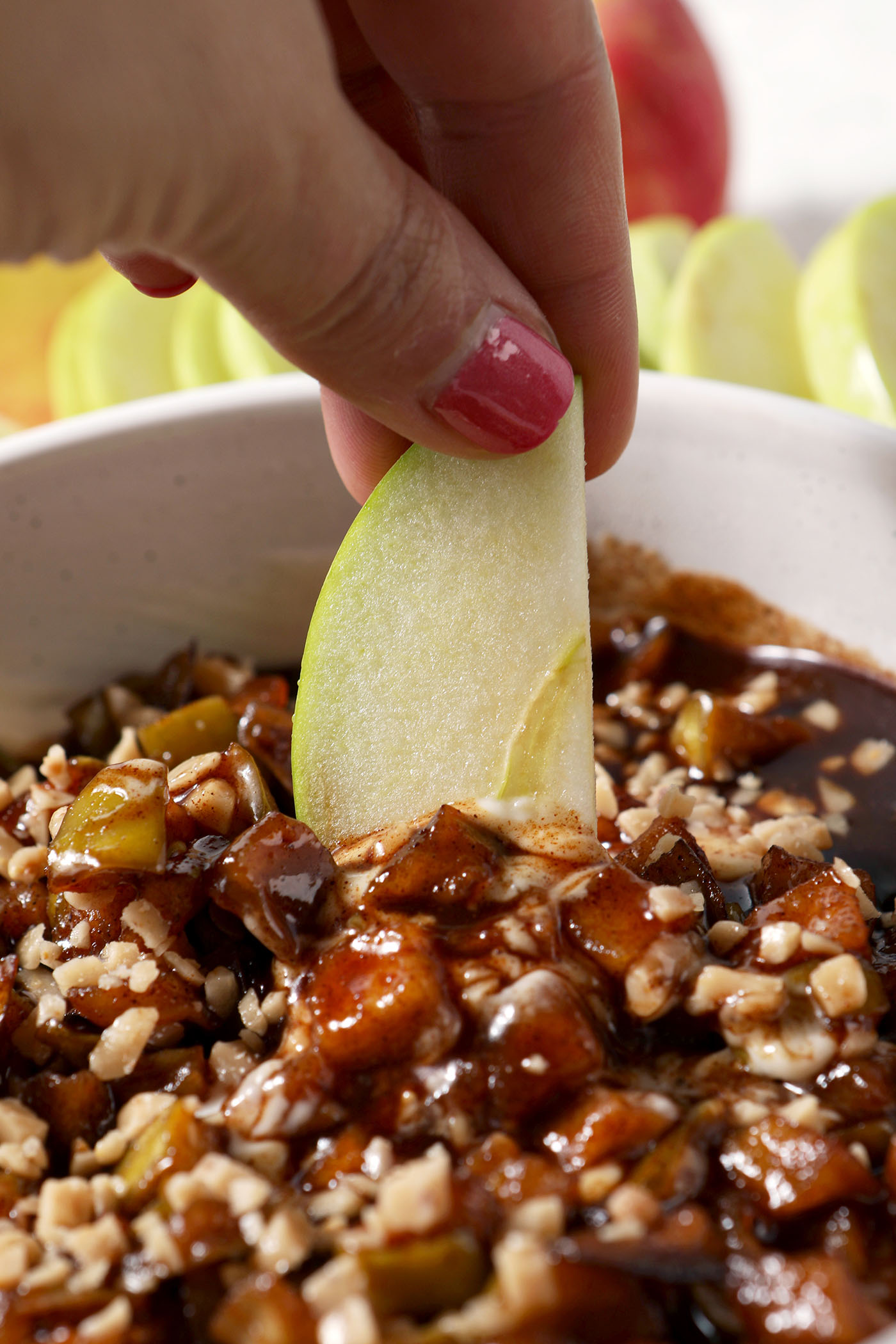An apple slice dips into a bowl of caramelized apple cheesecake dip