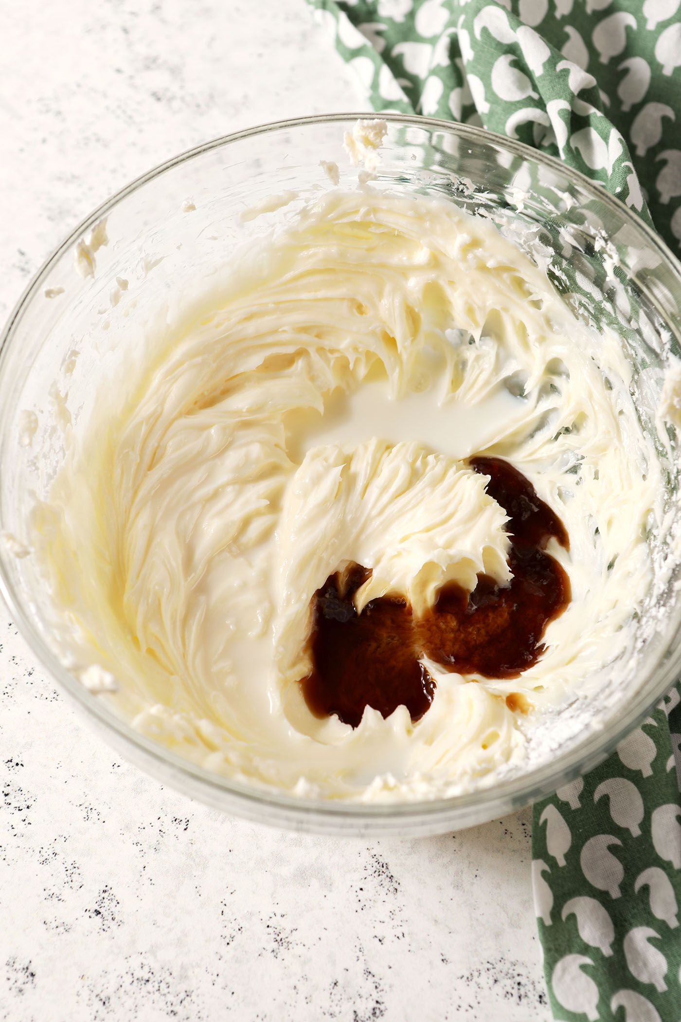 Vanilla extract and milk sit on top of a whipped cream cheese mixture in a bowl on a stone surface.