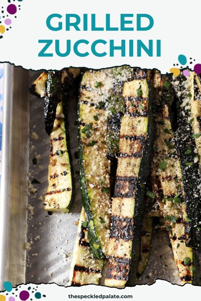 Close-up of grilled zucchini slices garnished with grated Parmesan and parsley on a silver sheet pan.