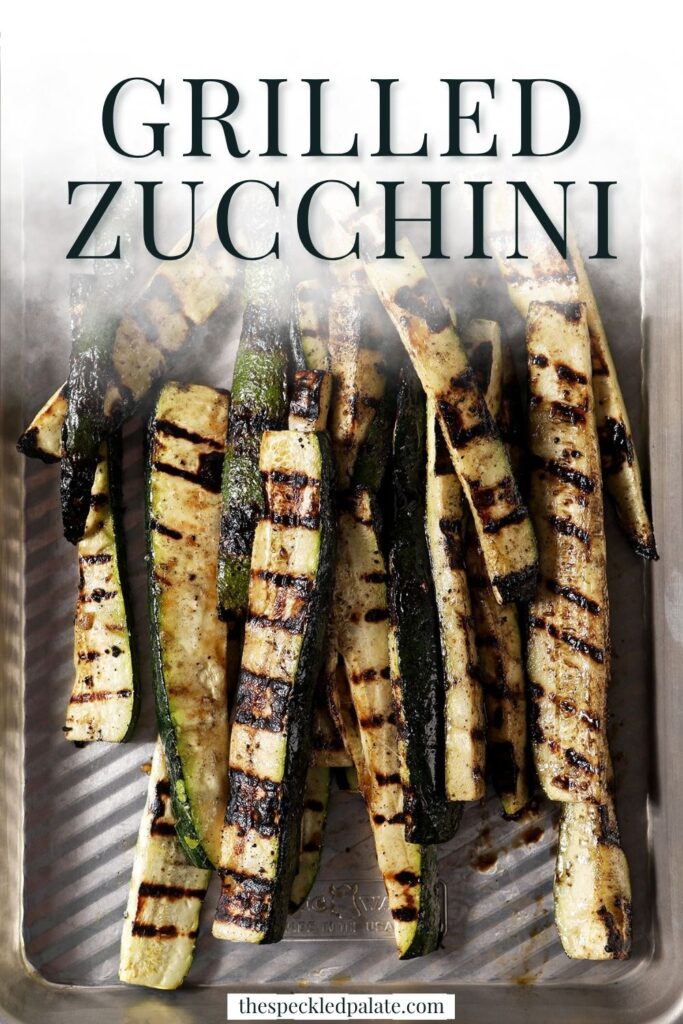 Close-up of grilled zucchini slices garnished with grated Parmesan and parsley on a silver sheet pan.