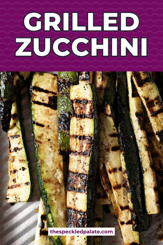 Close-up of grilled zucchini slices garnished with grated Parmesan and parsley on a silver sheet pan.