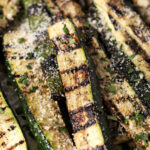 Side angle of grilled zucchini, garnished with grated Parmesan and parsley